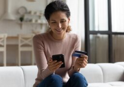 Mulher sorri com o cartão de crédito olhando para o celular